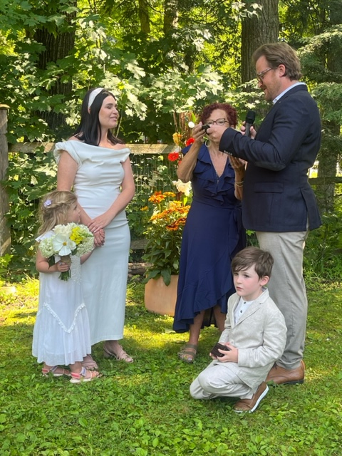 Sandra Ruch, wedding officiant, marrying bride and groom with child present in backyard setting